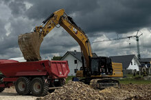 A 36-ton crawler excavator from Caterpillar loads excavated material into a red dump truck on a construction site.