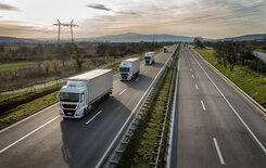 Several trucks drive at a perfect distance from each other as a platooning solution on the right lane of a highway.