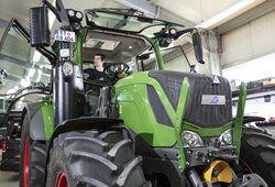 A light green tractor, retrofitted with NX NextMotion, is tested by a technician in the workshop while sitting in the cab.