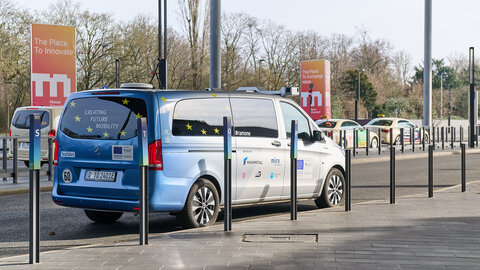 A blue and silver Mercedes van is parked on the roadside at the Düsseldorf Exhibition Centre. There are various logos on the car, such as Rheinmetall, Mira and Arnold NextG.